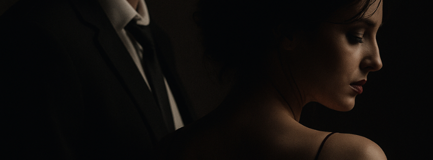 A dark, moody banner-style image in triptych form. On the left, a man in a black suit and tie is shown from the shoulders down, his face mostly hidden in shadow. In the center, a young woman in a black dress with a red ribbon on her arm looks down with a somber expression. On the right, the same woman is shown in close-up profile with eyes closed, softly illuminated against a shadowed background.